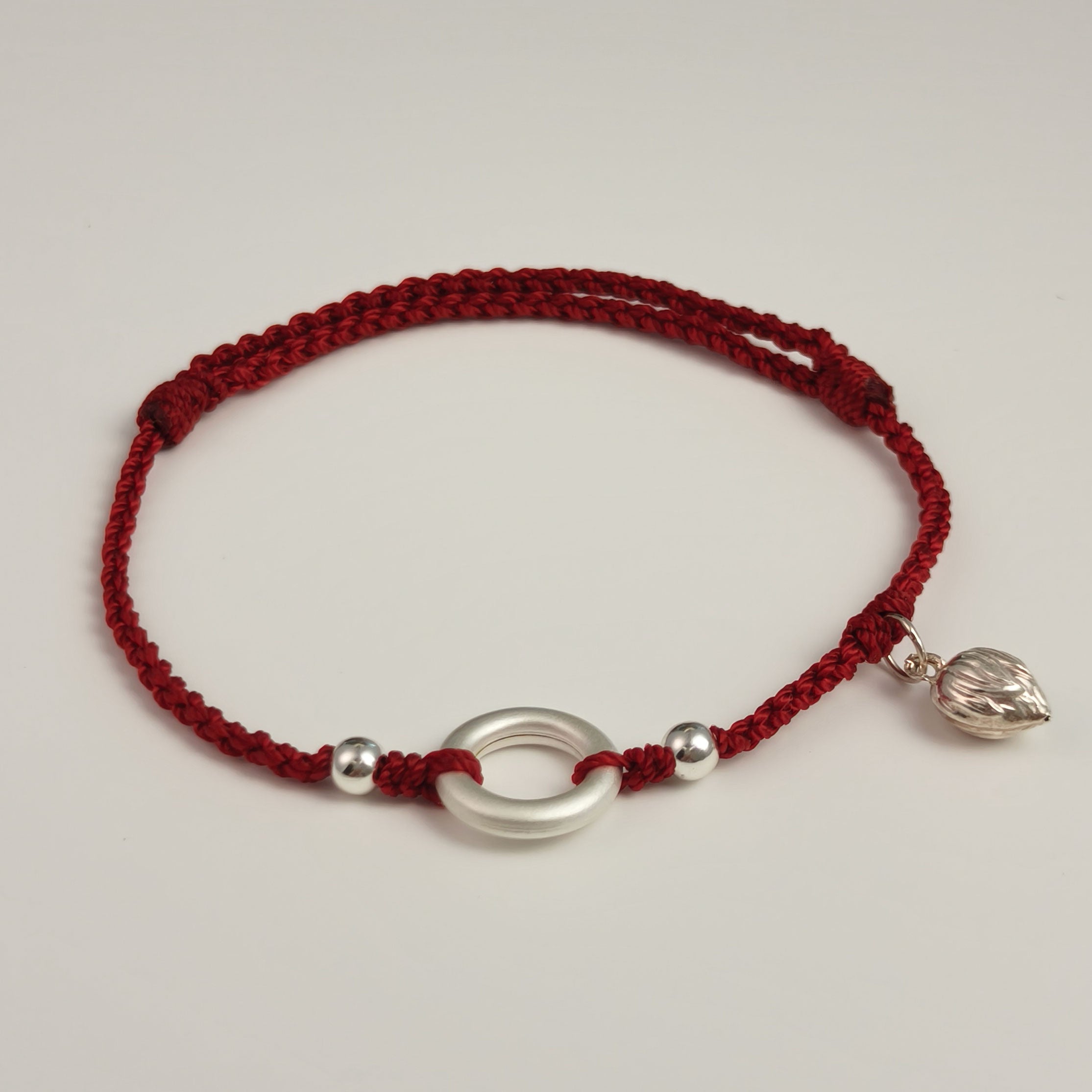 Handwoven red string bracelet with silver ring and lotus charm, symbol of protection and renewal.