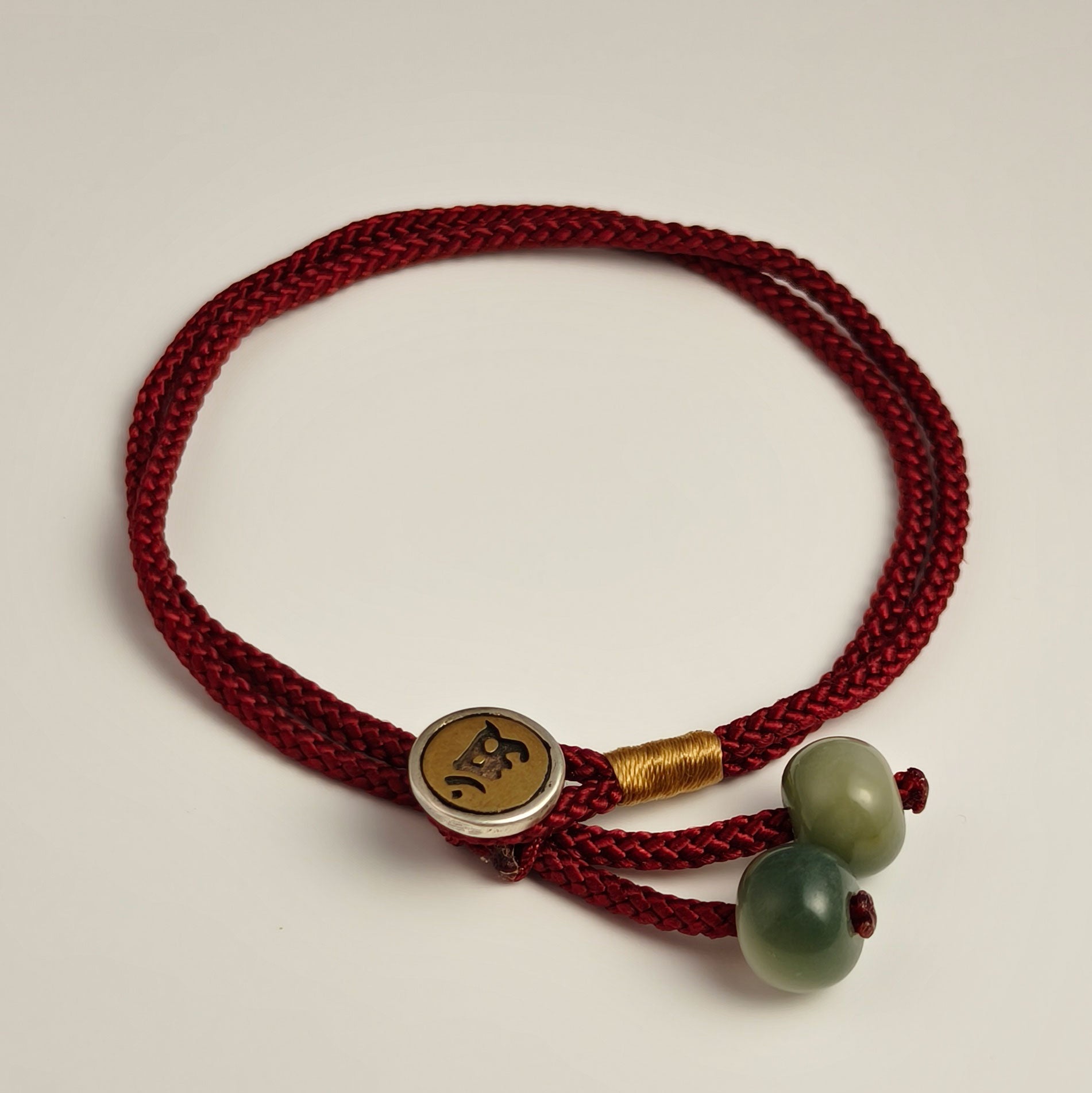 Red string bracelet with engraved metal clasp and green bodhi seed, symbol of protection and harmony.