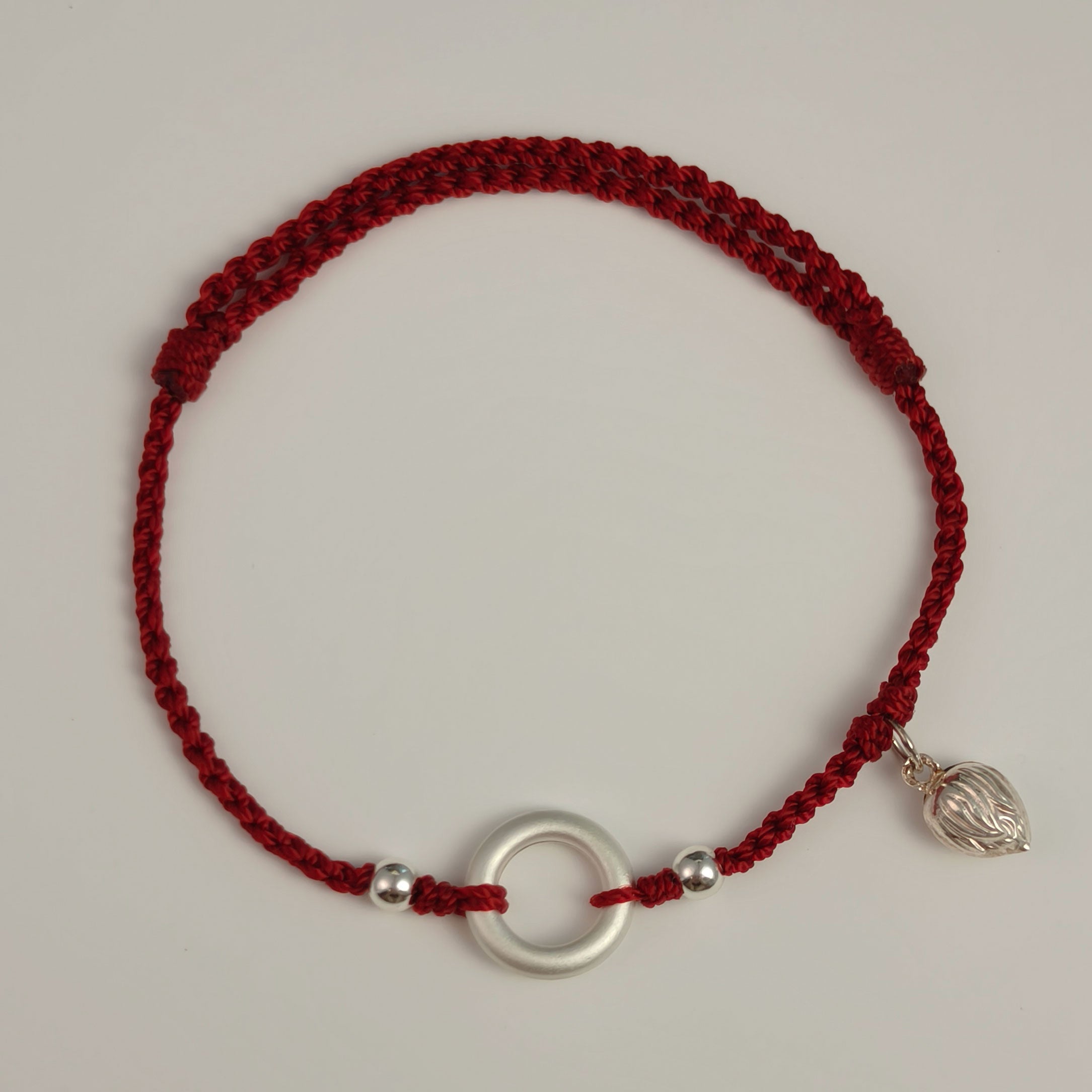 Red string bracelet with silver circle and lotus charm, handwoven for meaning and protection.