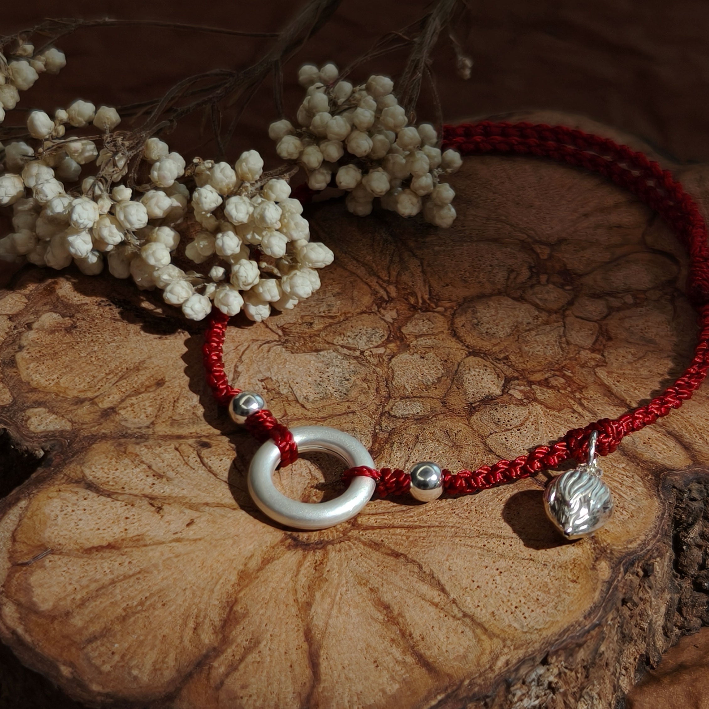 Red string bracelet with silver ring and lotus charm, symbolizing protection and renewal.